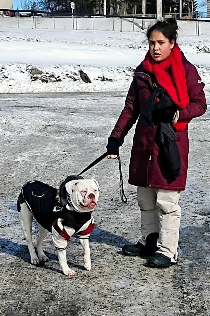 Kristine walking Coco on a lead along a snowy road, Coco wearing a black winter coat.